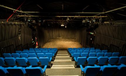 Image of a black box studio theatre with rows of blue seats