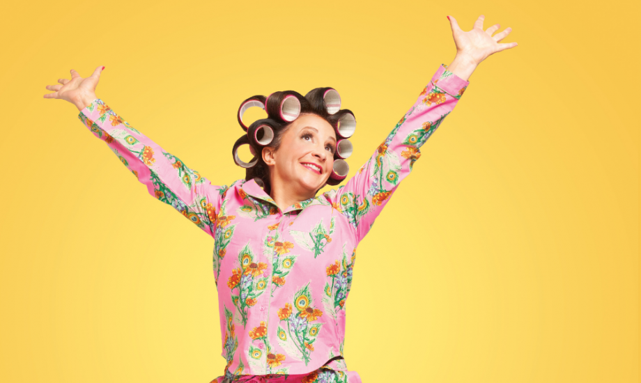 Lucy Porter jumping for joy in front of a sunshine yellow background in her pyjamas.