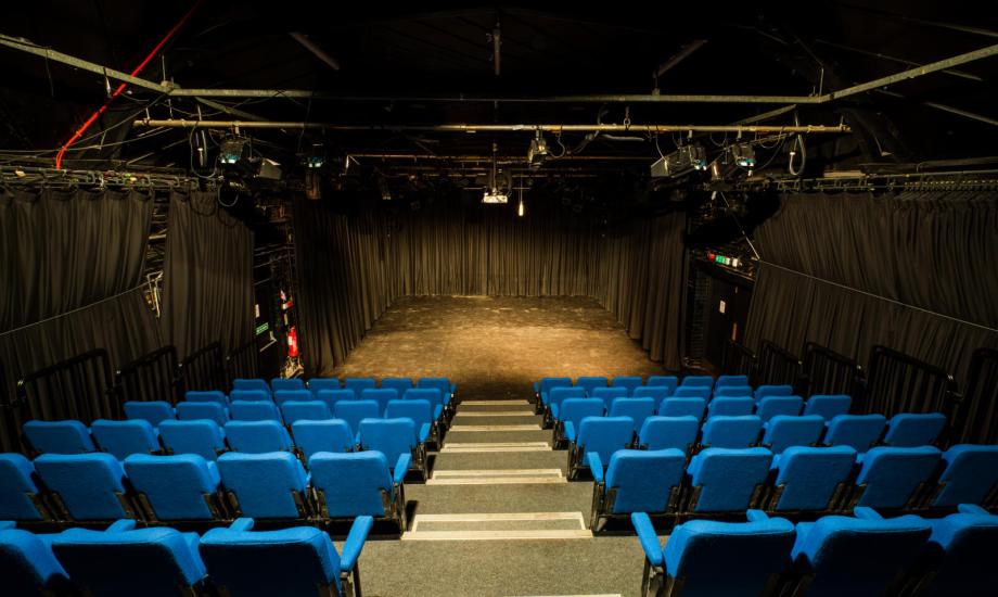 Image of a black box studio theatre with rows of blue seats